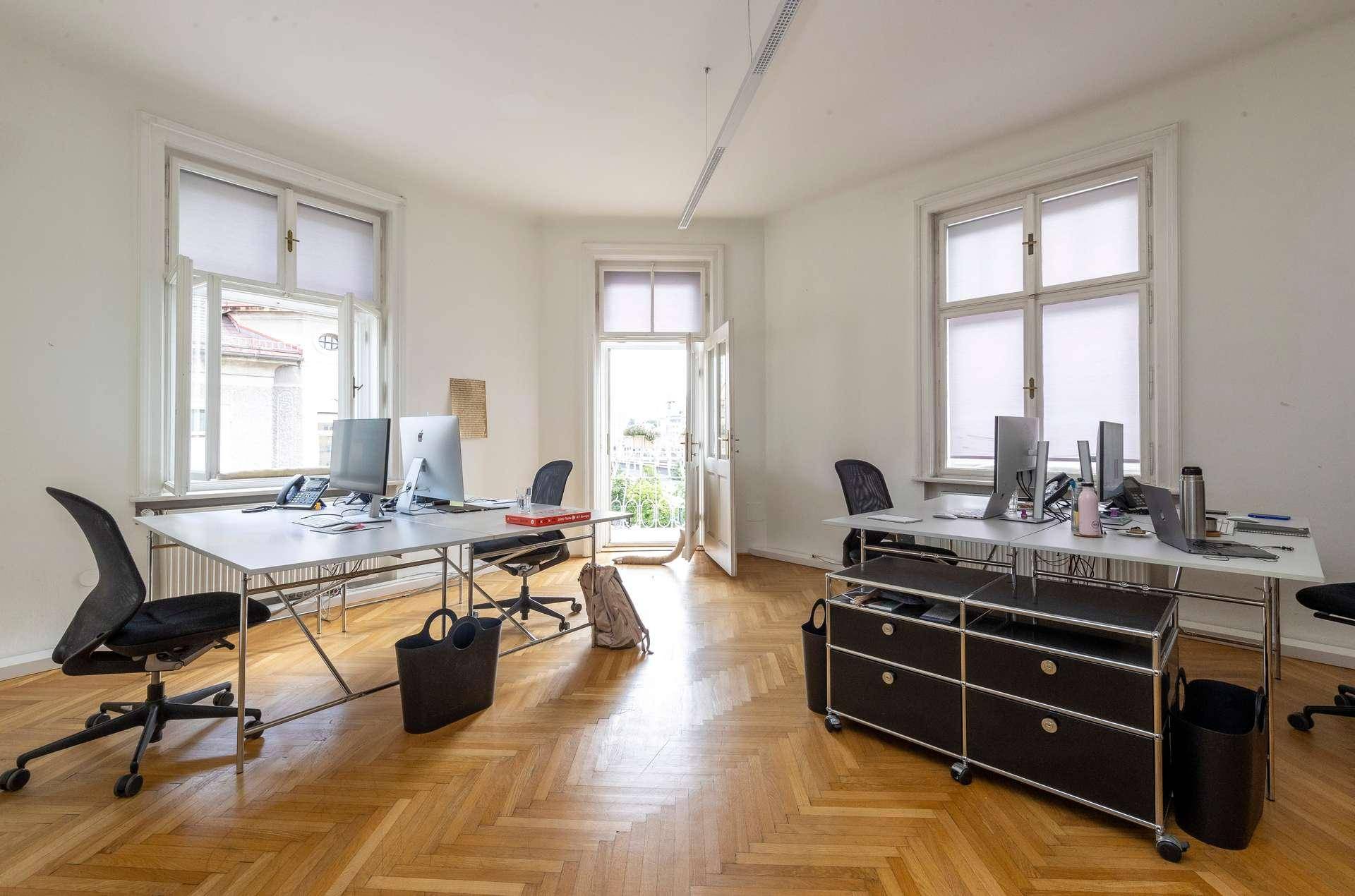 Großes Büro mit mehreren Arbeitsplätzen, Computern und Zugang zu einem Balkon, der viel Licht hereinlässt.