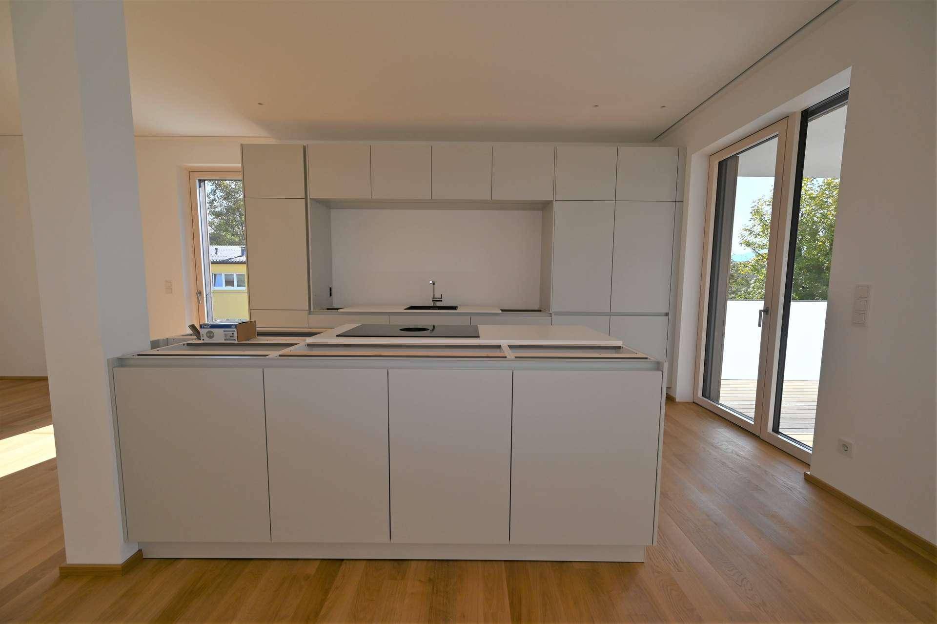 Moderne Küche im Bau mit weißer Kücheninsel und Schränken, ausgestattet mit Induktionskochfeld und Holzboden.