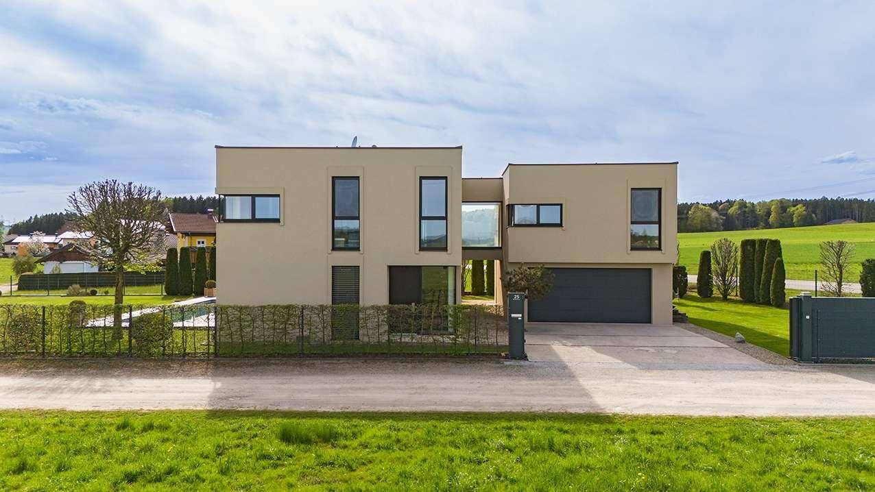 Frontansicht der modernen Villa mit integrierter Doppelgarage und großzügiger Auffahrt, umgeben von Natur.
