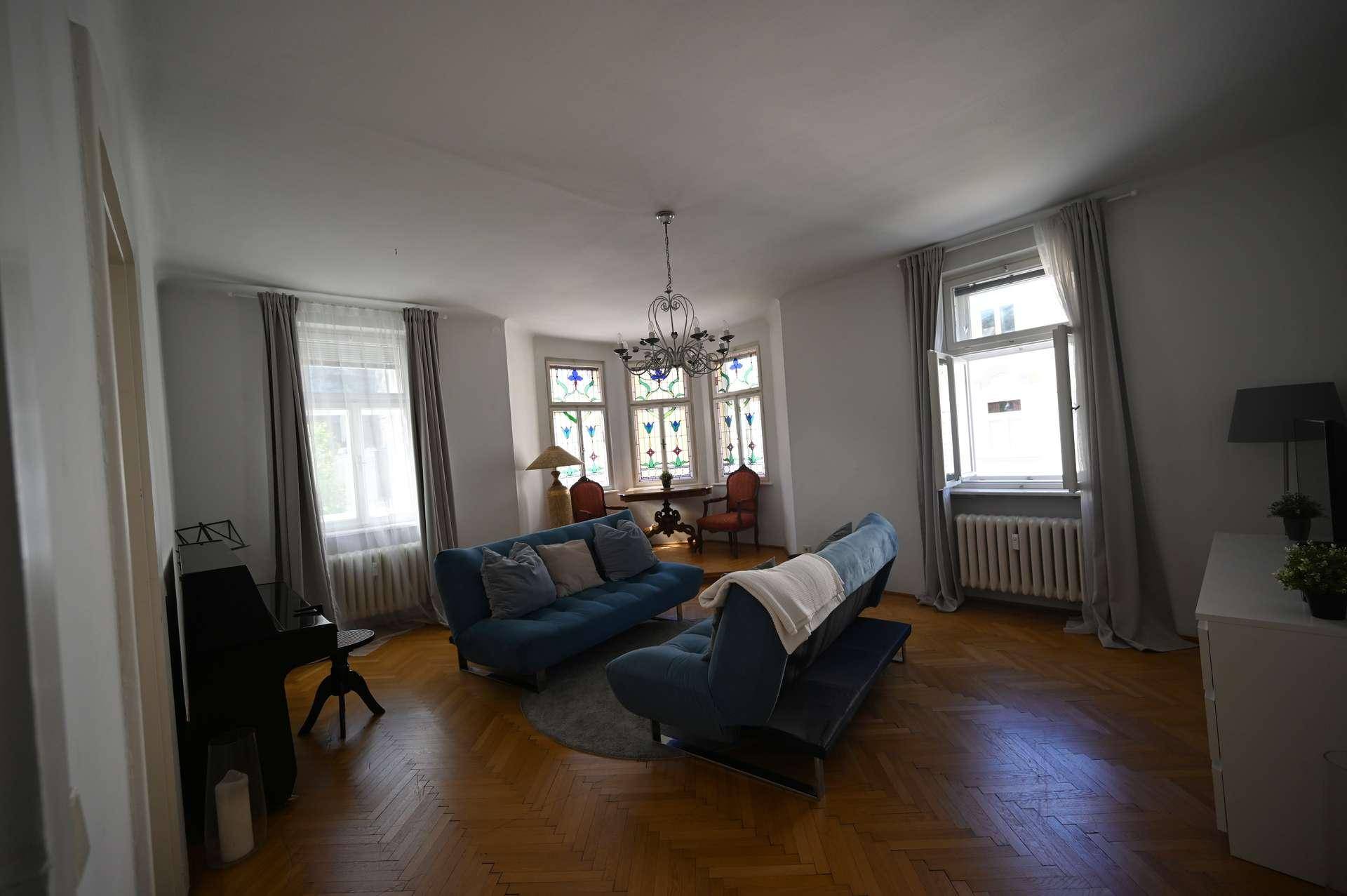 Geräumiges Wohnzimmer mit zwei blauen Sofas, Kronleuchter und Fischgrätparkett.