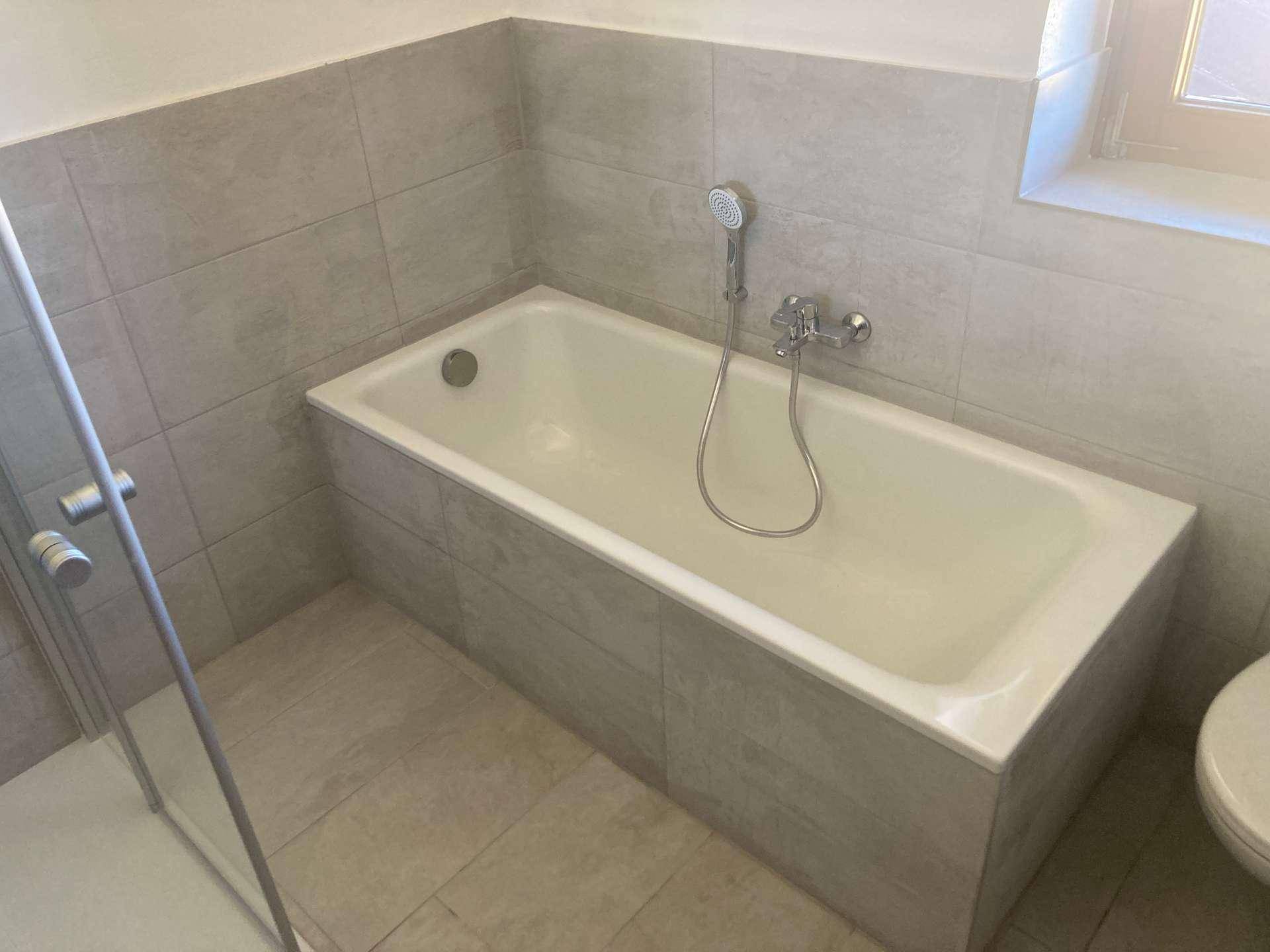 Badezimmer mit Badewanne und modernen grauen Fliesen, gut gepflegt.