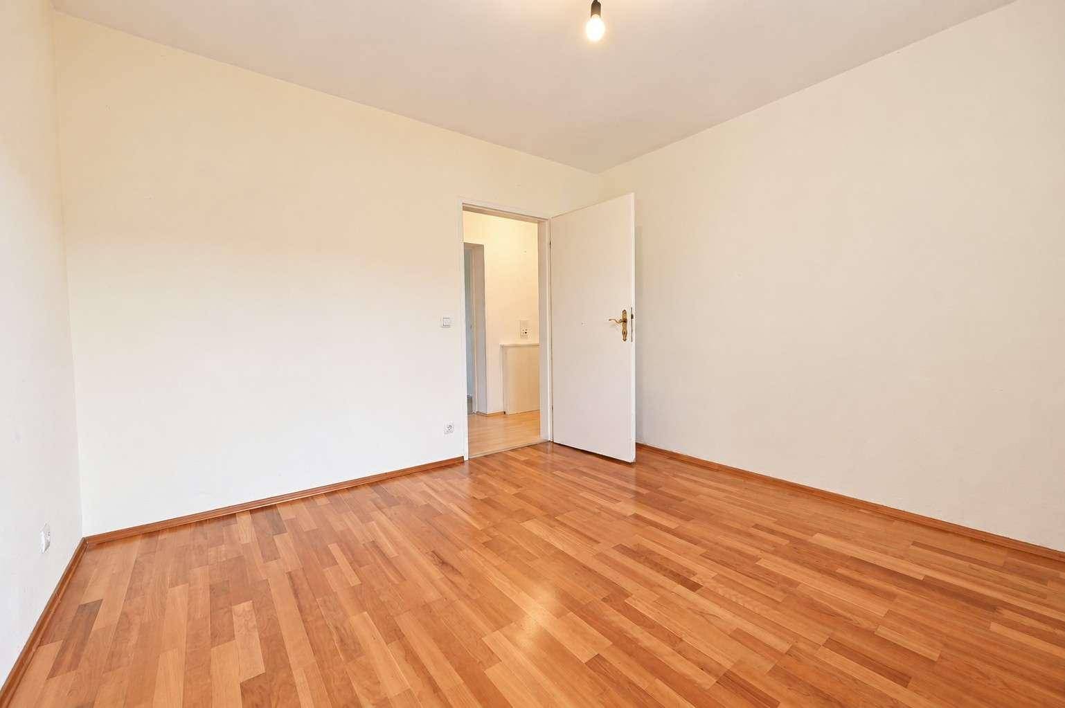 Leeres Zimmer mit hellem Holzplankenboden und Zugang zu einem weiteren Raum.