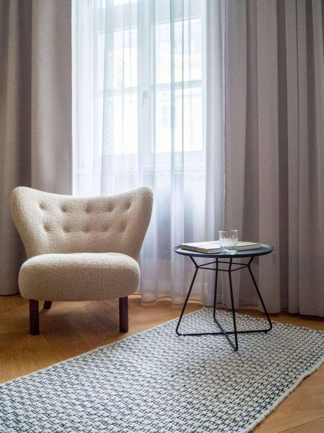 Gemütlicher Sessel mit Beistelltisch vor einem großen Fenster mit Vorhängen.