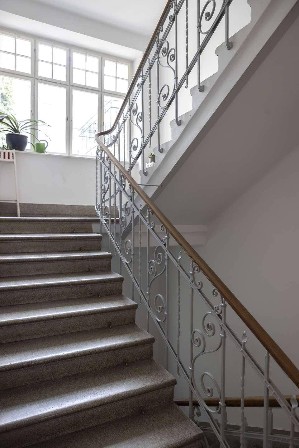 Elegantes Treppenhaus mit schmiedeeisernem Geländer und großen Fenstern.