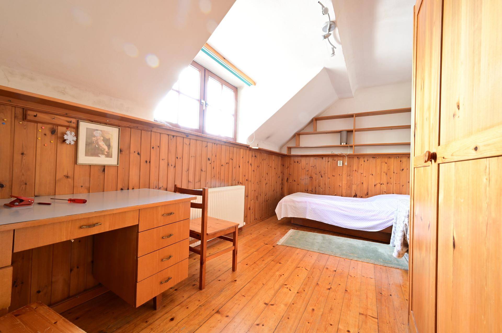 Gemütliches Dachzimmer mit Holzboden, Holzvertäfelung, Bett, Schreibtisch und Dachfenster.