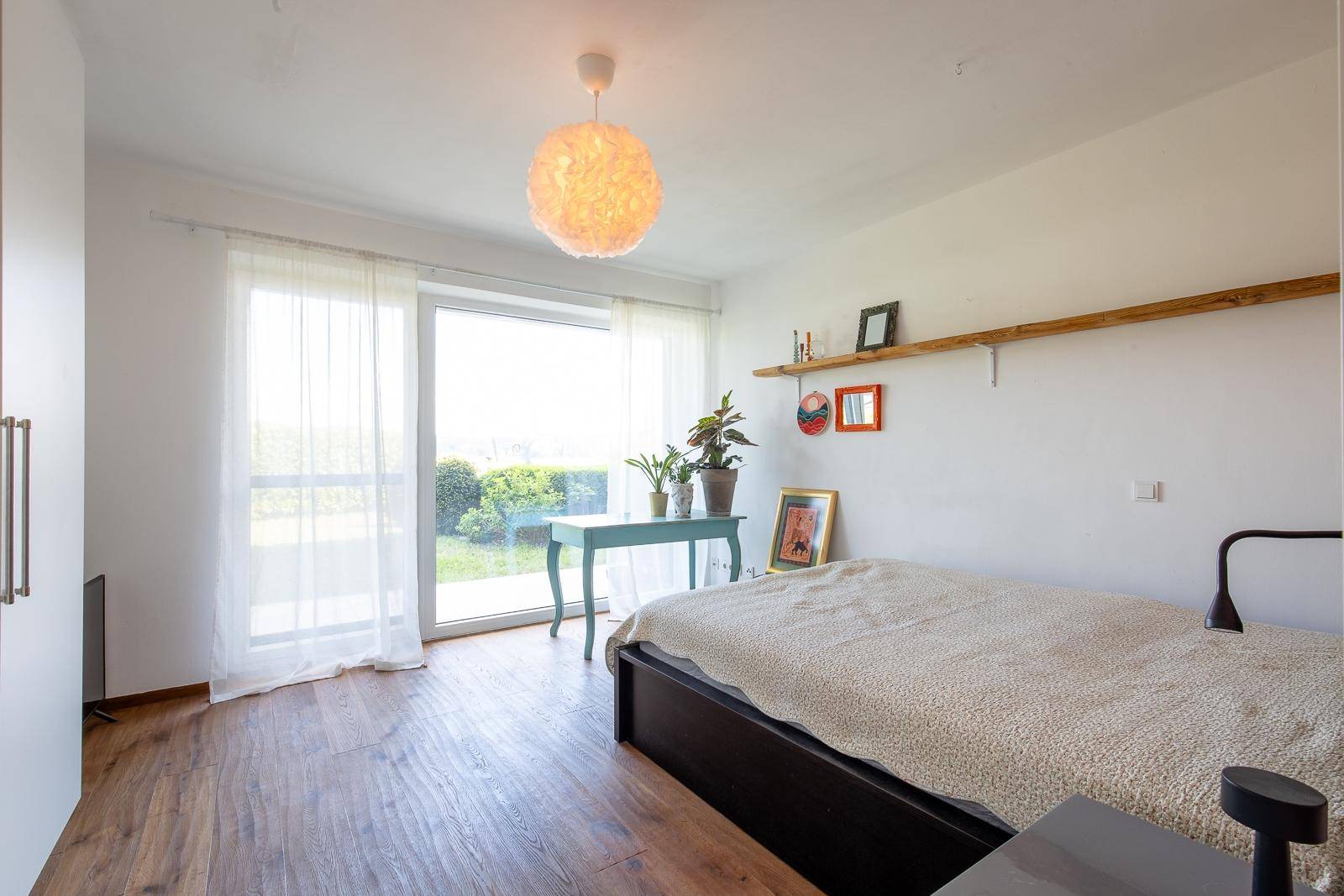 Helles Schlafzimmer mit Holzboden, großem Fenster und Zugang zu einem Außenbereich.