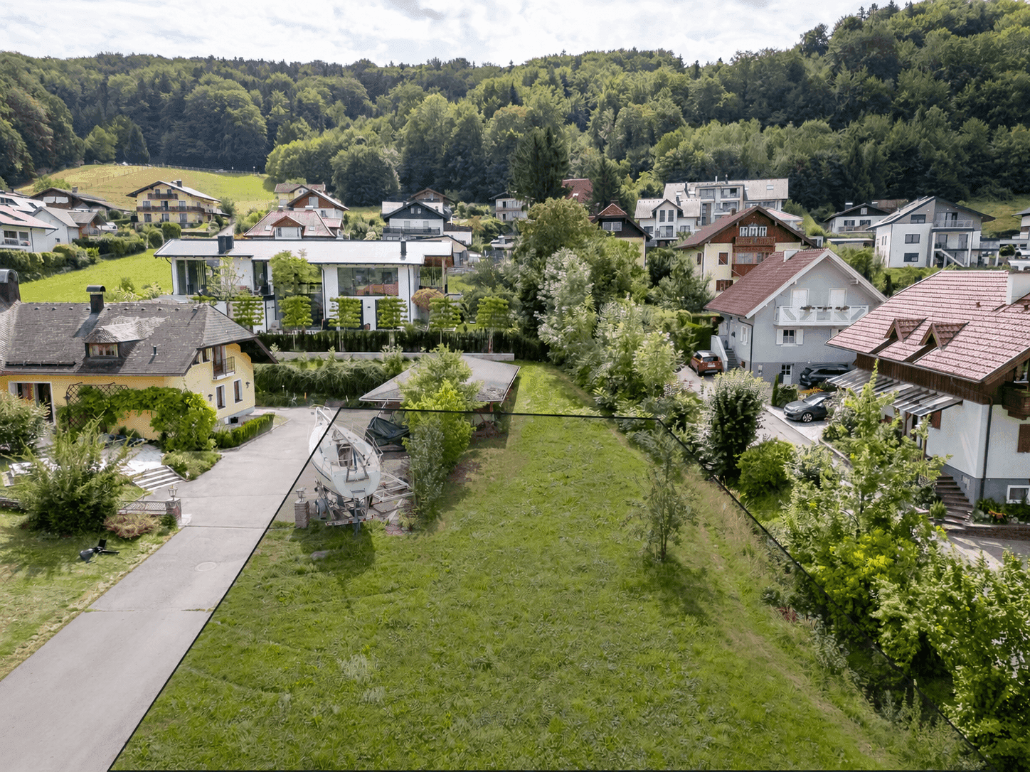 Luftaufnahme eines grünen Baugrundstücks mit klarer Umrandung, umgeben von Wohnhäusern und üppiger Vegetation.