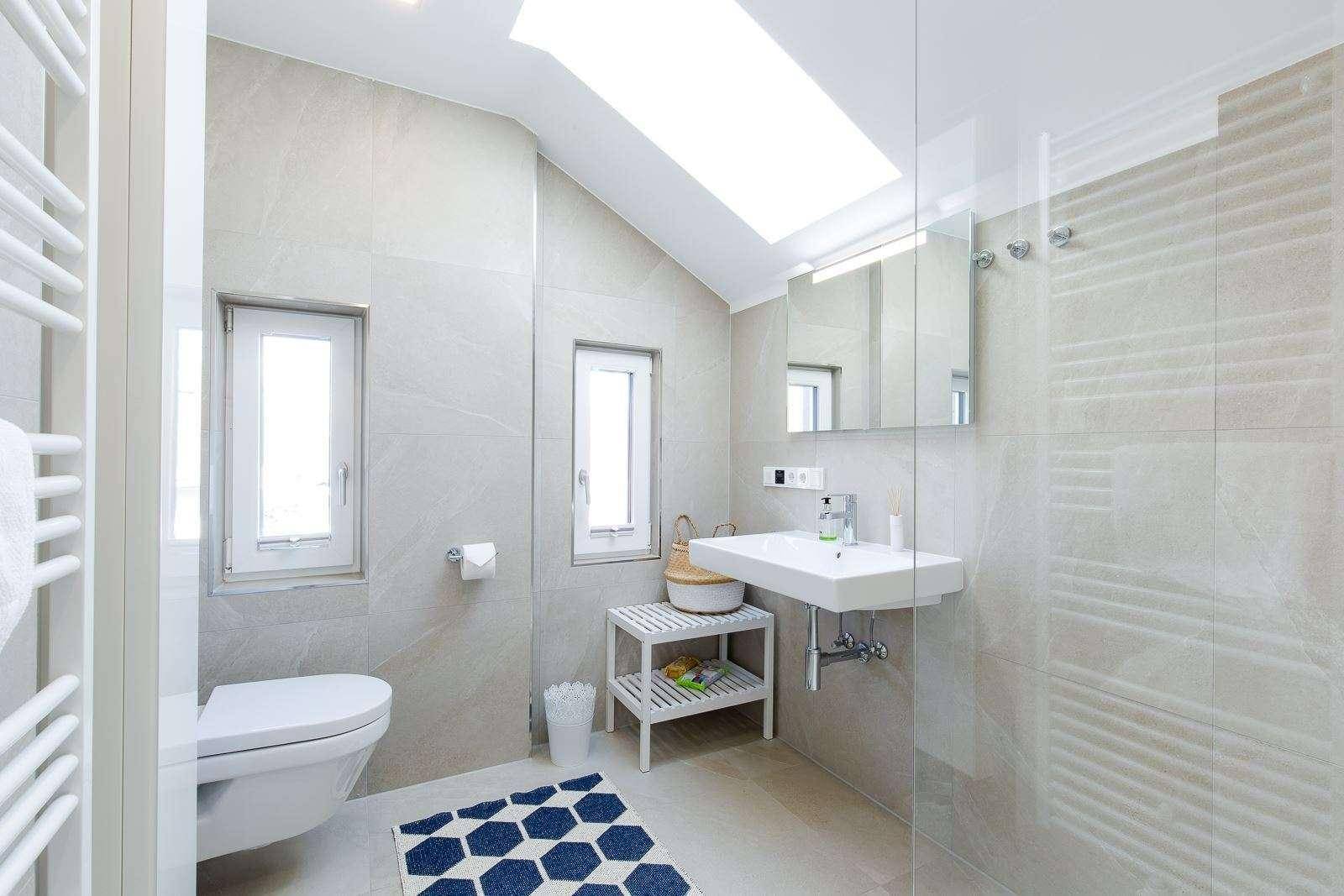 Modernes Badezimmer mit hellen Fliesen, begehbarer Dusche und Dachfenster für viel Licht.