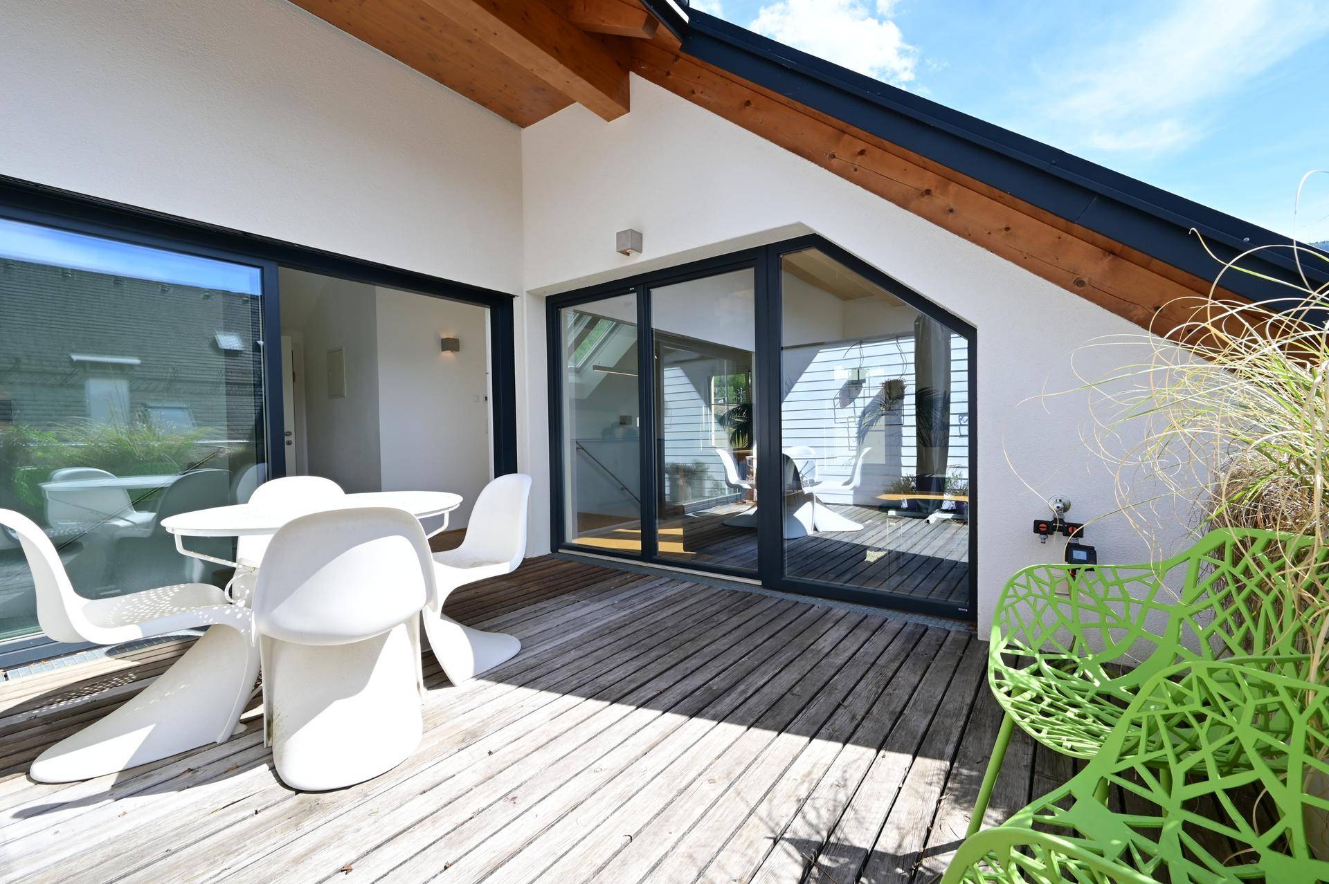Geräumige Holzterrasse mit modernen Gartenmöbeln und direktem Zugang zum Innenbereich durch große Glasfronten.