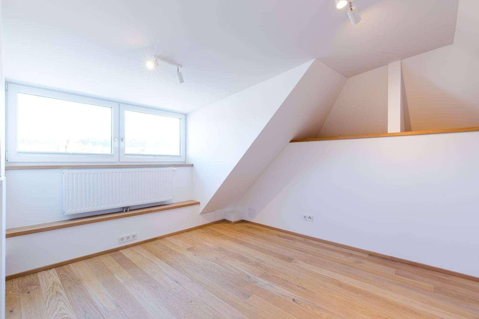 Heller Raum im Dachgeschoss mit Holzboden, schrägen Wänden und großen Fenstern.