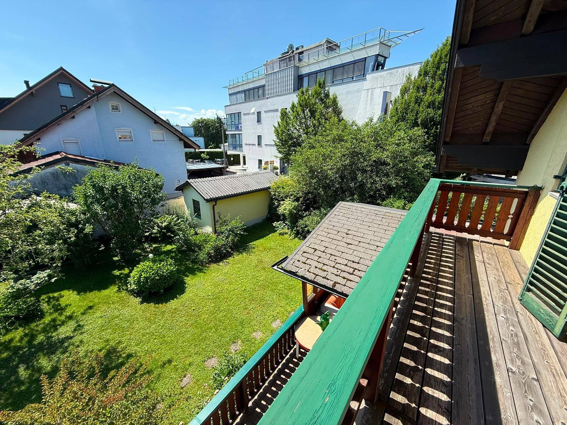 Balkon mit Blick auf den gepflegten Garten, Bäume und umliegende Gebäude.