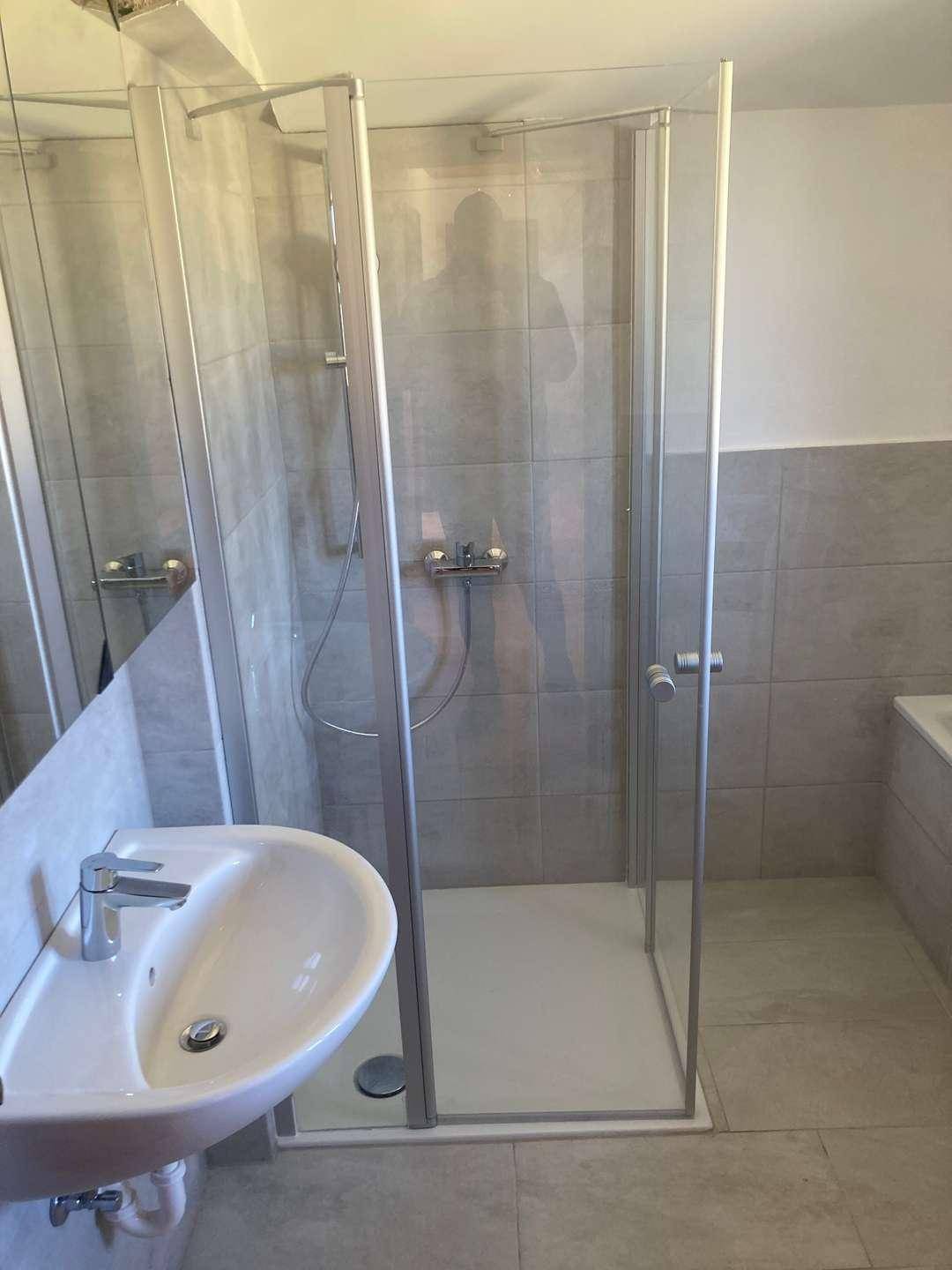 Modernes Badezimmer mit Duschkabine, Einzelwaschbecken und hellgrauen Fliesen.