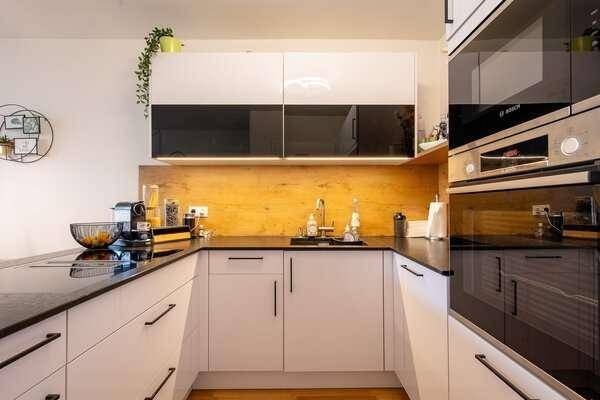 Detailansicht der modernen Küche mit weißen Schränken, schwarzen Arbeitsplatten und integrierten Geräten.