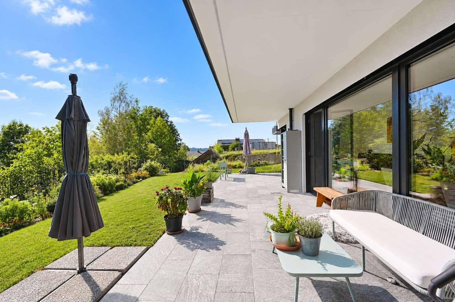 Große gepflasterte Terrasse mit Gartenmöbeln und weitem Blick über den Garten und die Landschaft.