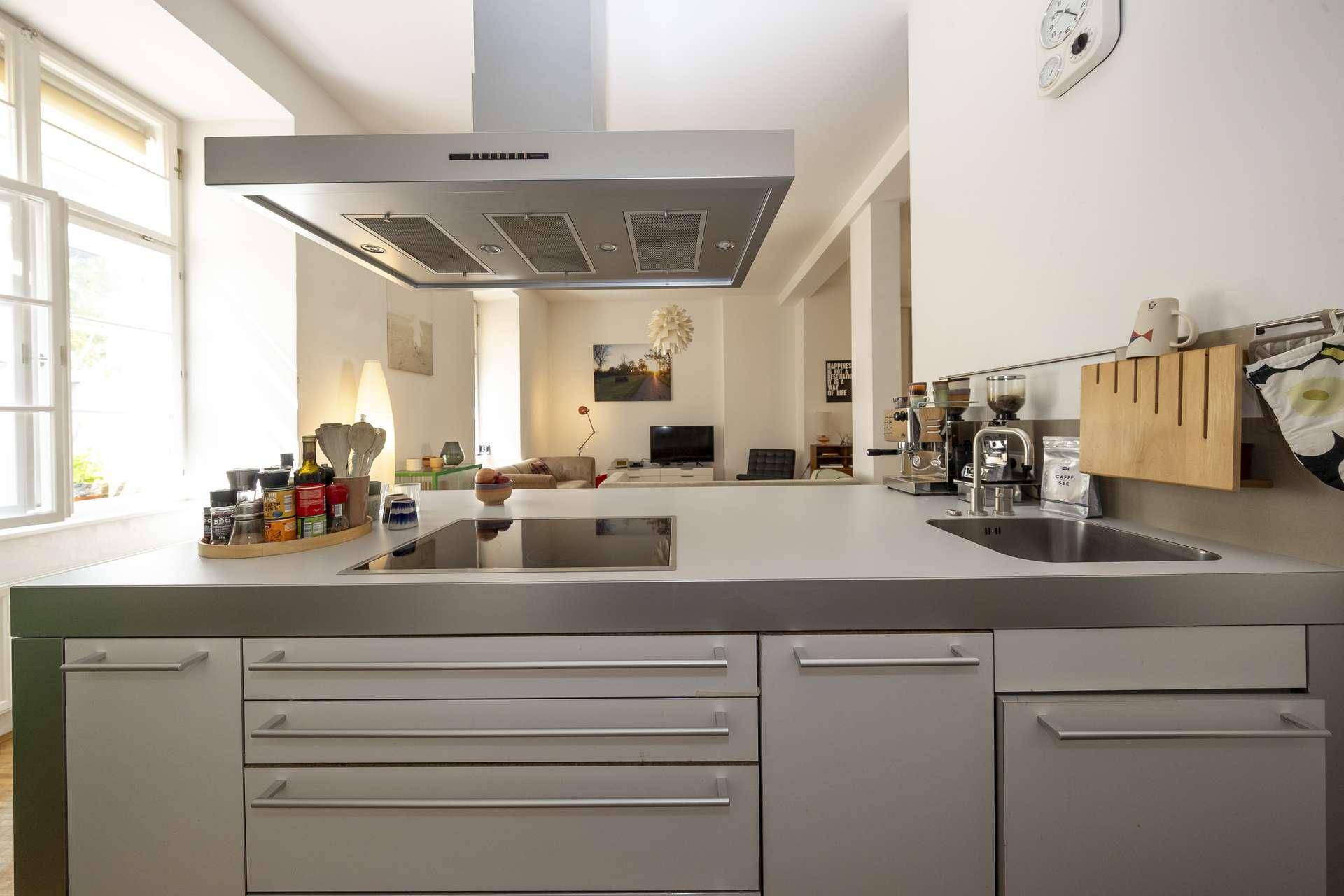 Offene Küche mit Edelstahl-Arbeitsplatte und Spüle, bietet Blick auf den angrenzenden Wohnbereich.