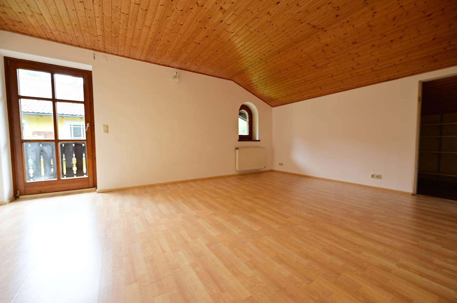 Gemütliches Zimmer mit Holzdecke, Laminatboden und einem charmanten Rundbogenfenster.