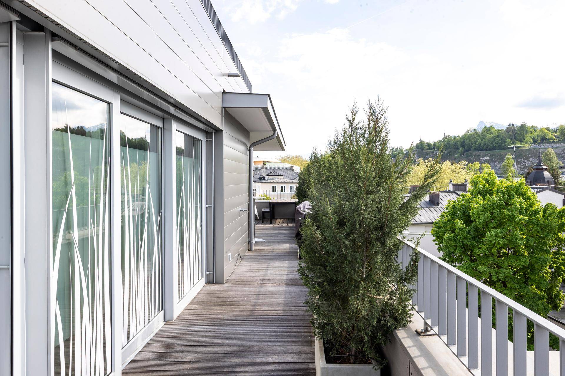 Schmale Terrasse mit Holzboden, Pflanzen und Blick auf die Umgebung.