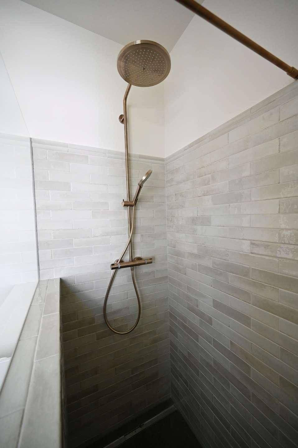 Moderne Dusche mit Regenduschkopf und hellgrauen Fliesen in Ziegeloptik.