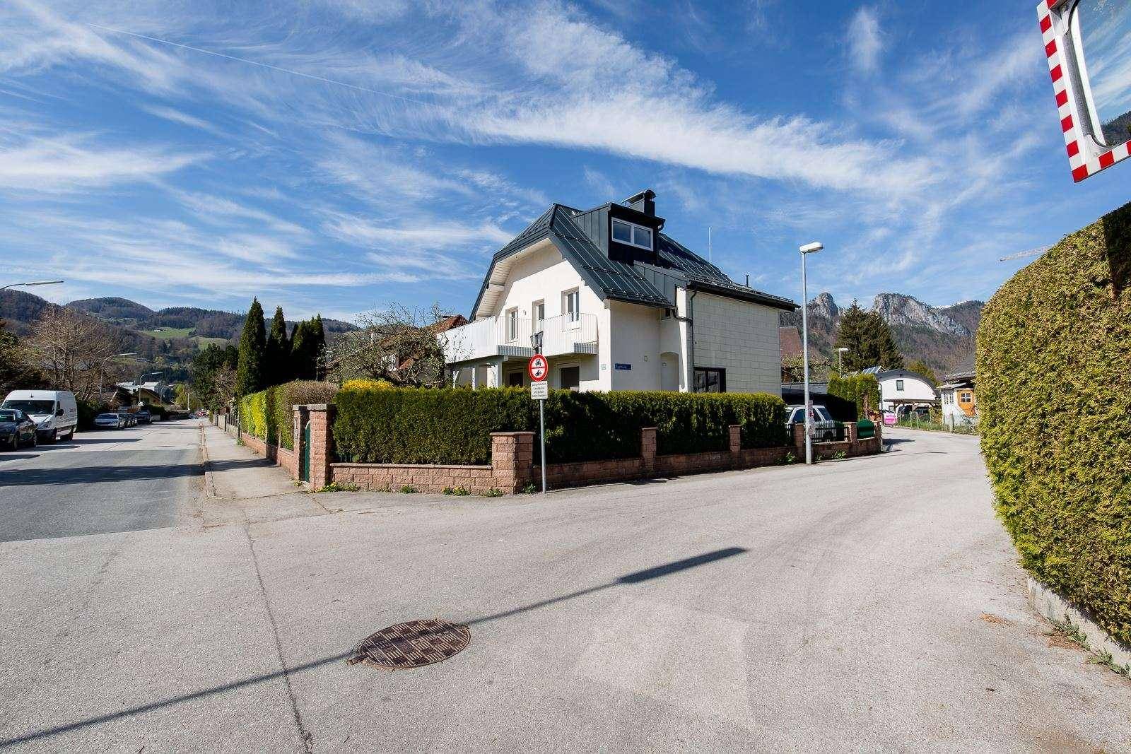 Wohnhaus an einer Straße mit gepflegter Hecke und Bergblick im Hintergrund.