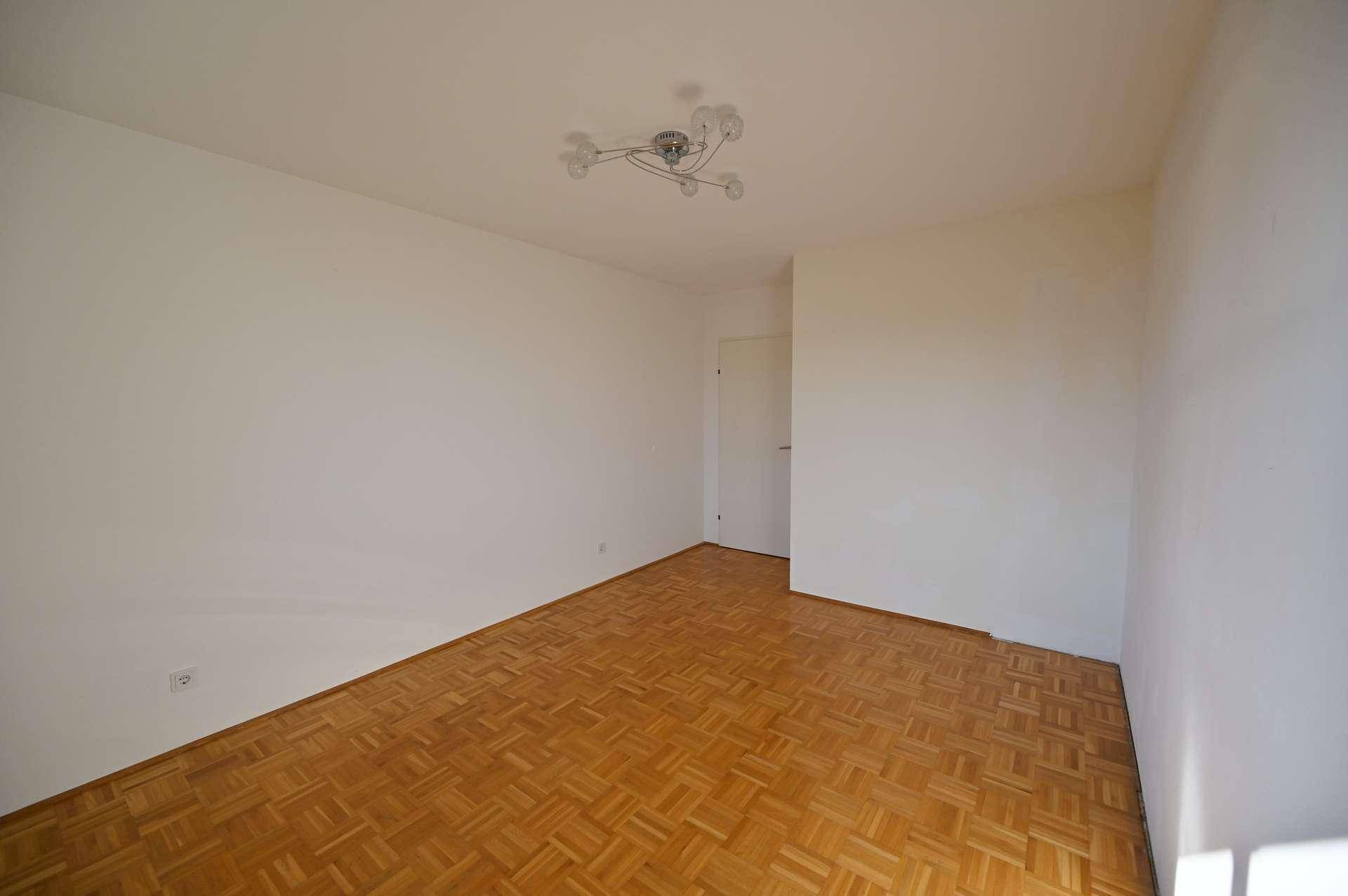 Helles Schlafzimmer mit Parkettboden und weißen Wänden, bereit zur individuellen Gestaltung.