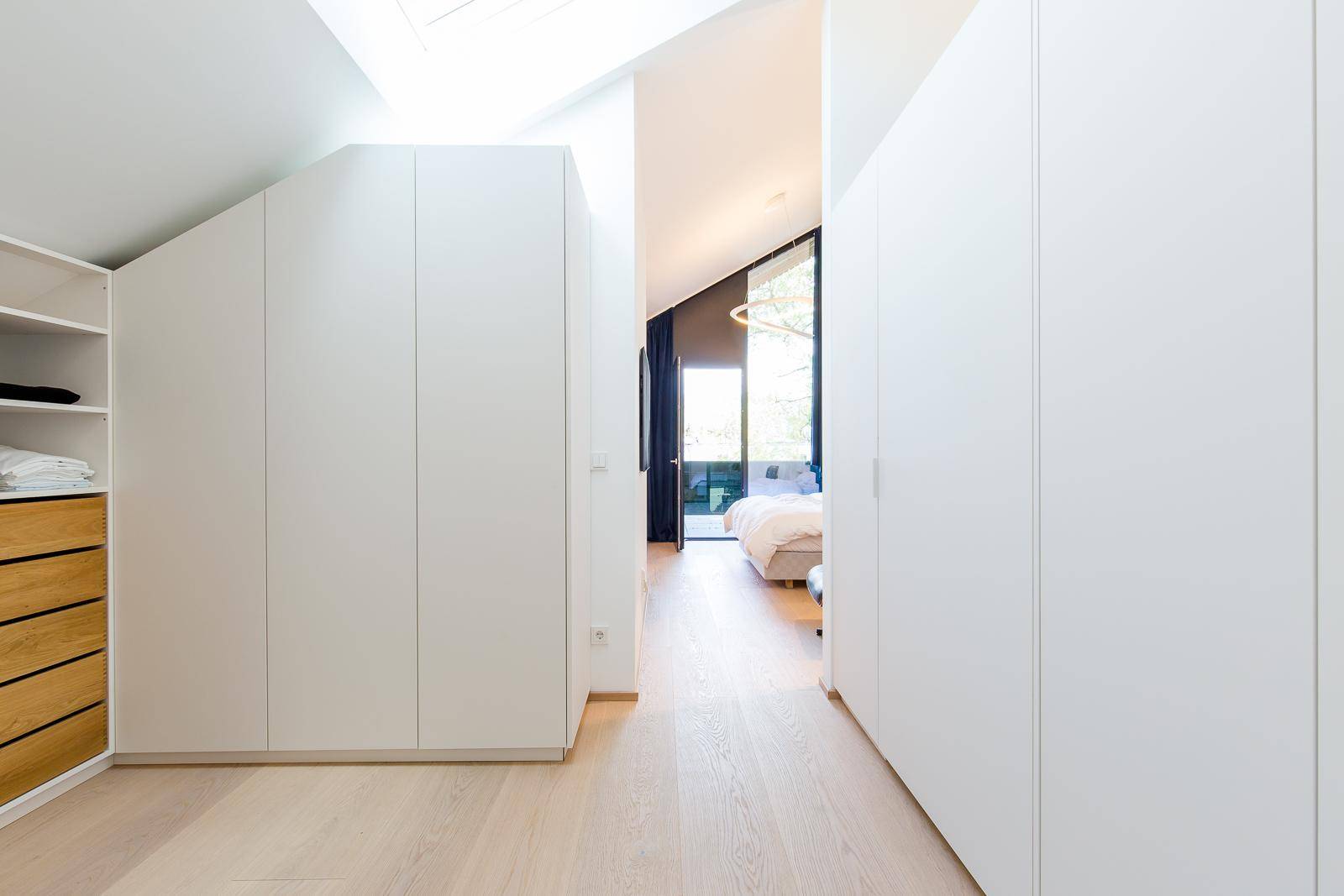 Heller Flur mit Einbauschränken und Zugang zu einem Schlafzimmer mit Dachschräge.