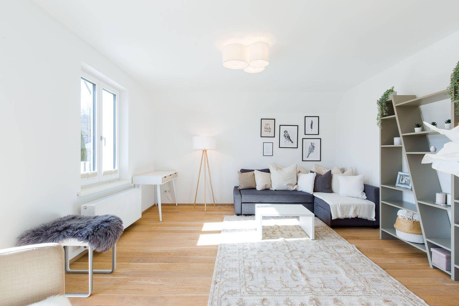 Geräumiges Wohnzimmer mit Holzboden, Sofa, Teppich und großen Fenstern für viel Licht.