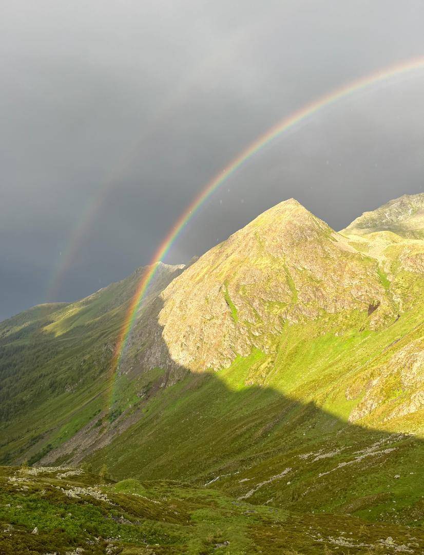 Beeindruckende Berglandschaft mit einem leuchtenden Regenbogen, der sich über die grünen Hänge spannt.