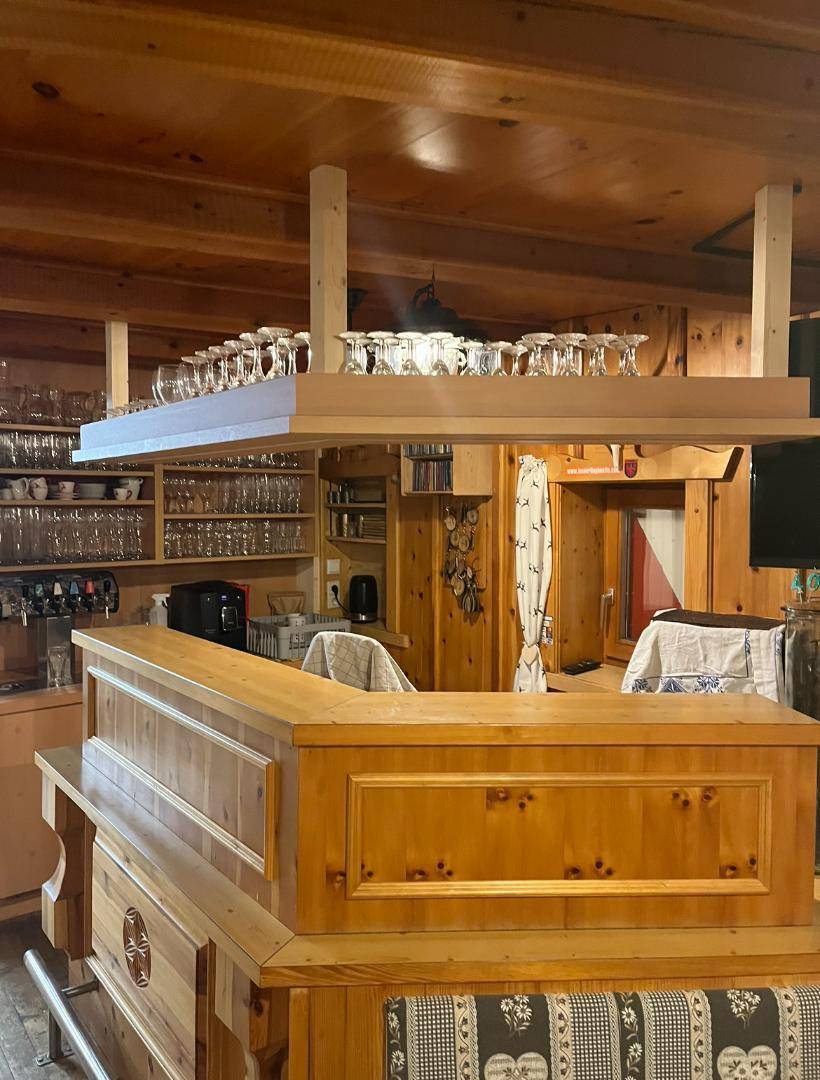 Rustikale Holzbar mit Gläsern und Regalen, typisch für eine Berghütte oder ein Gasthaus.