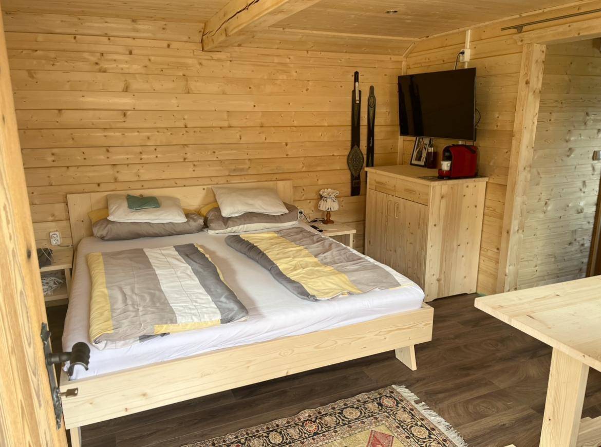 Schlichtes Schlafzimmer in einer Holzhütte mit Doppelbett, Holzwänden und einem Fernseher.