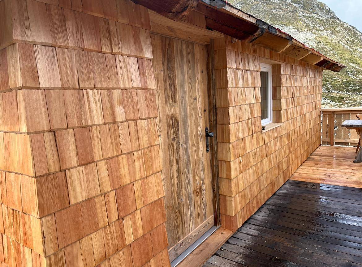 Nahaufnahme einer neuen Holzfassade mit Schindeln und einer Holztür, die zu einem Gebäude führt.