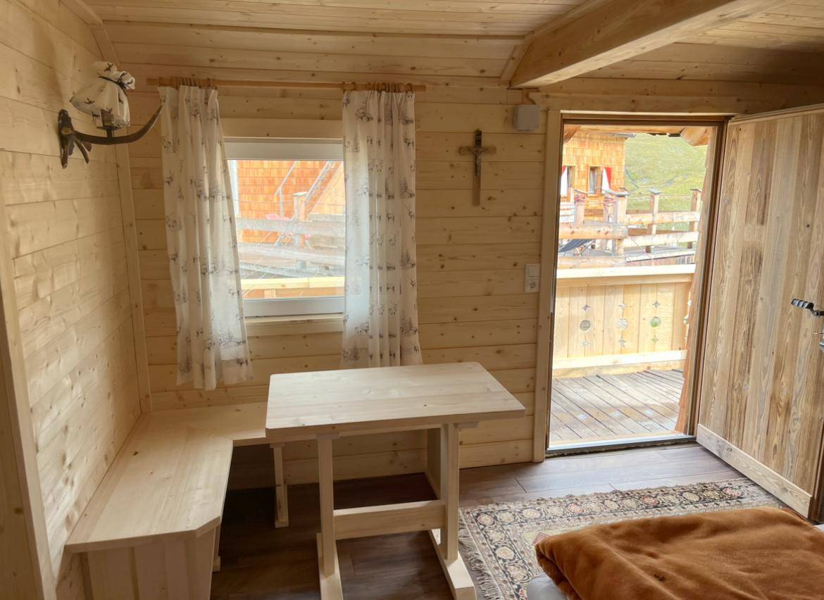Gemütlicher Essbereich in einer Holzhütte mit Holzbänken, Tisch und Zugang zu einer Außenterrasse.