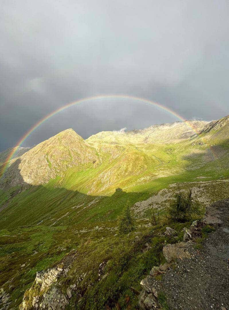 Malerische Berglandschaft mit einem Regenbogen, der sich über die grünen Gipfel und Täler erstreckt.