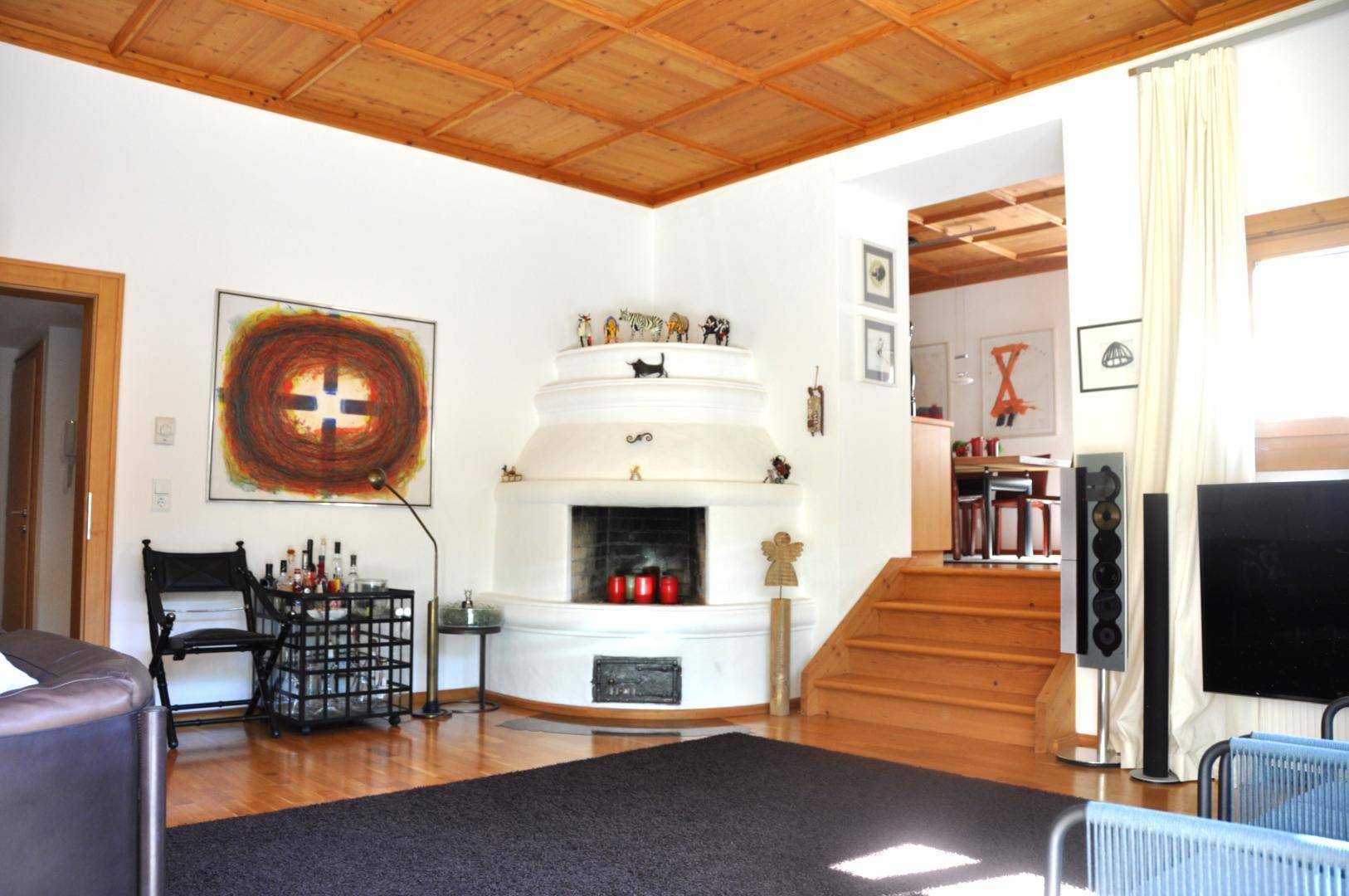 Gemütliches Wohnzimmer mit traditionellem Kachelofen, Holzbalkendecke und Parkettboden.