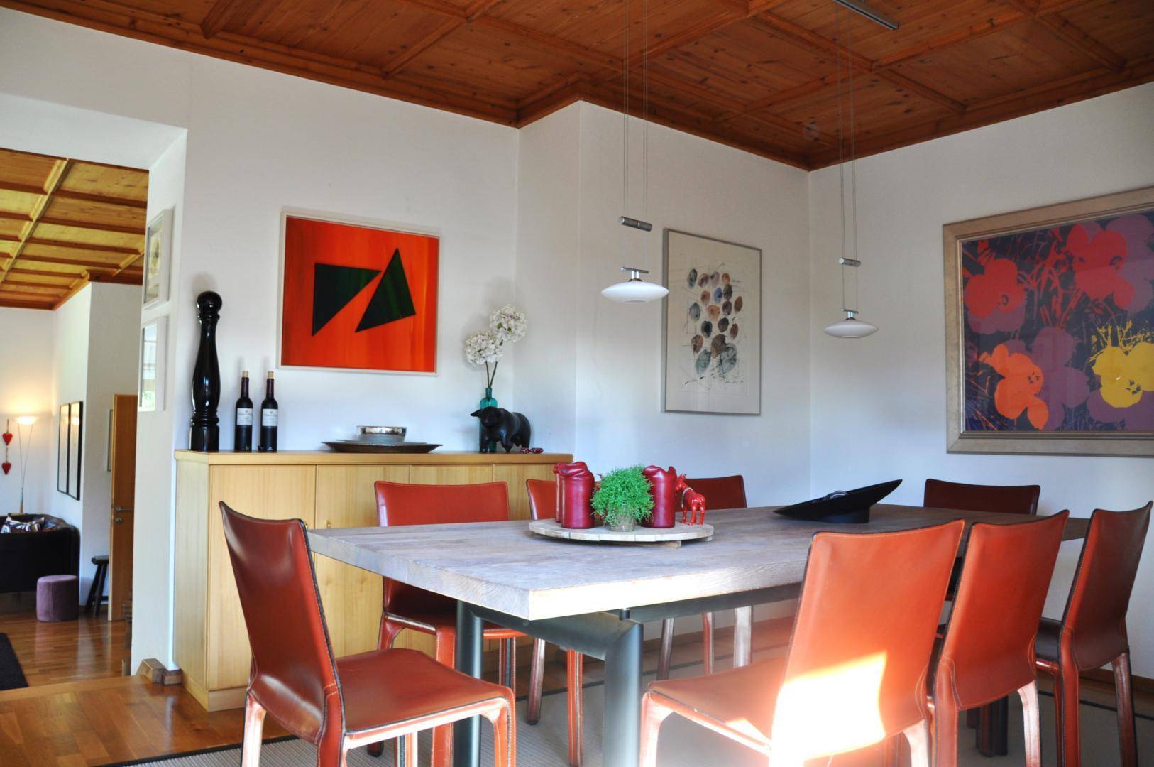 Geräumiger Essbereich mit großem Holztisch, modernen Kunstwerken und Holzbalkendecke.