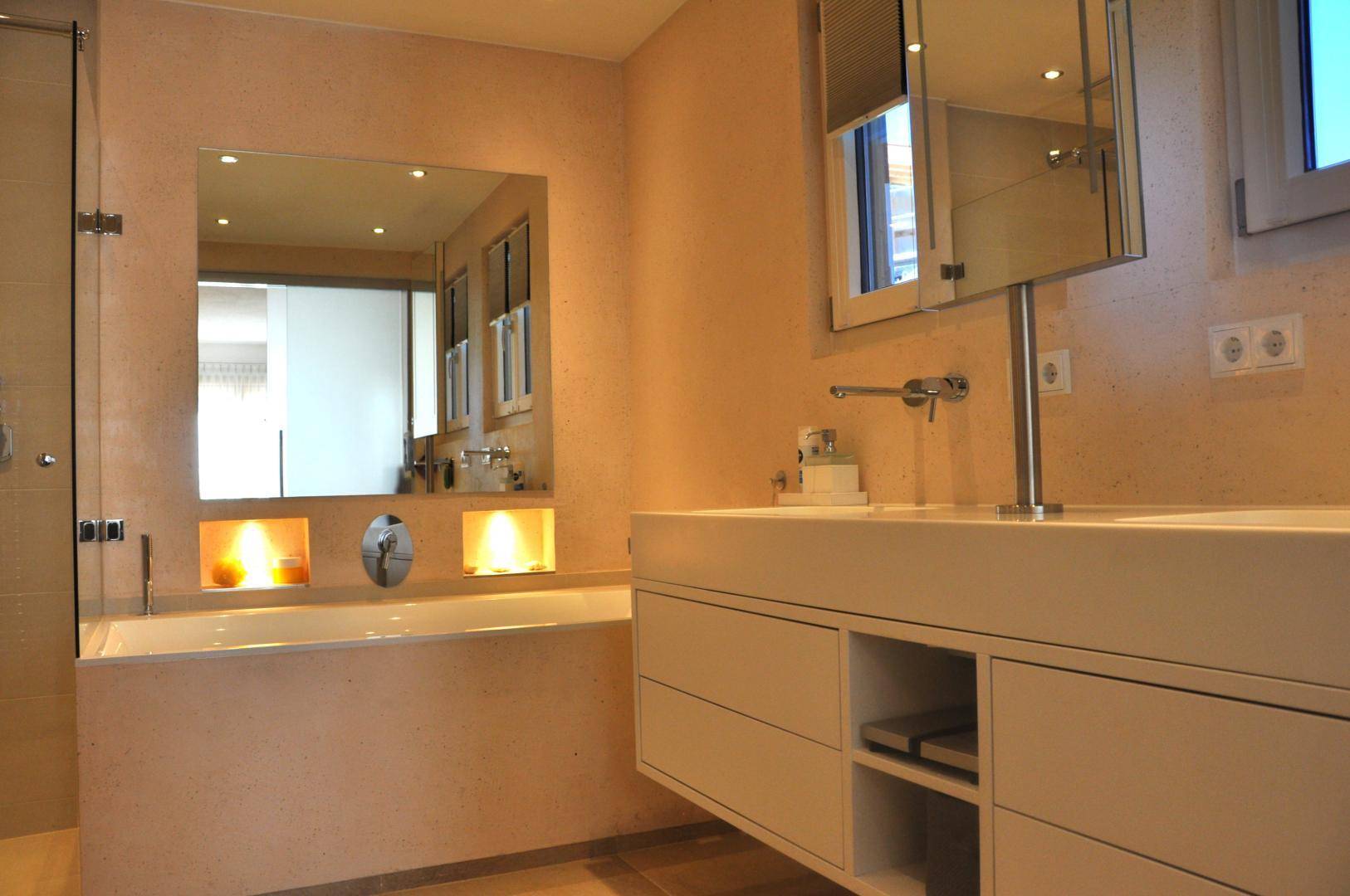 Modernes Badezimmer mit Badewanne, Doppelwaschbecken und beleuchteten Nischen für eine angenehme Atmosphäre.