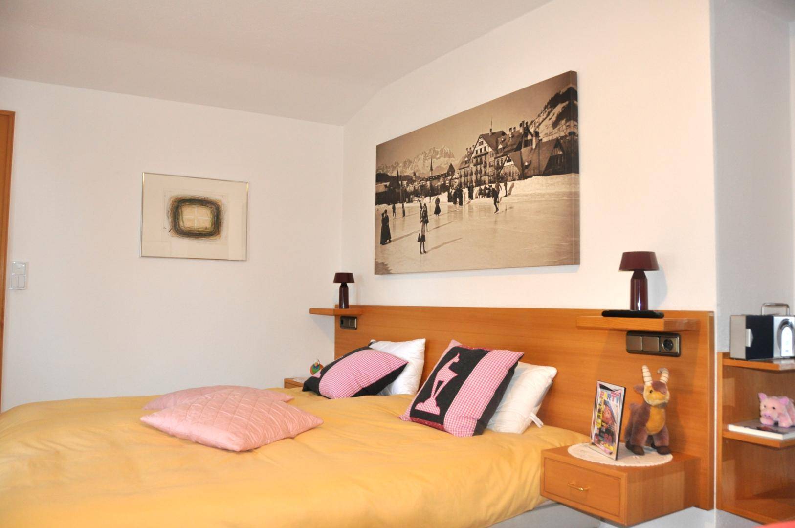 Helles Schlafzimmer mit großem Wandbild über dem Bett und praktischen Nachttischen aus Holz.