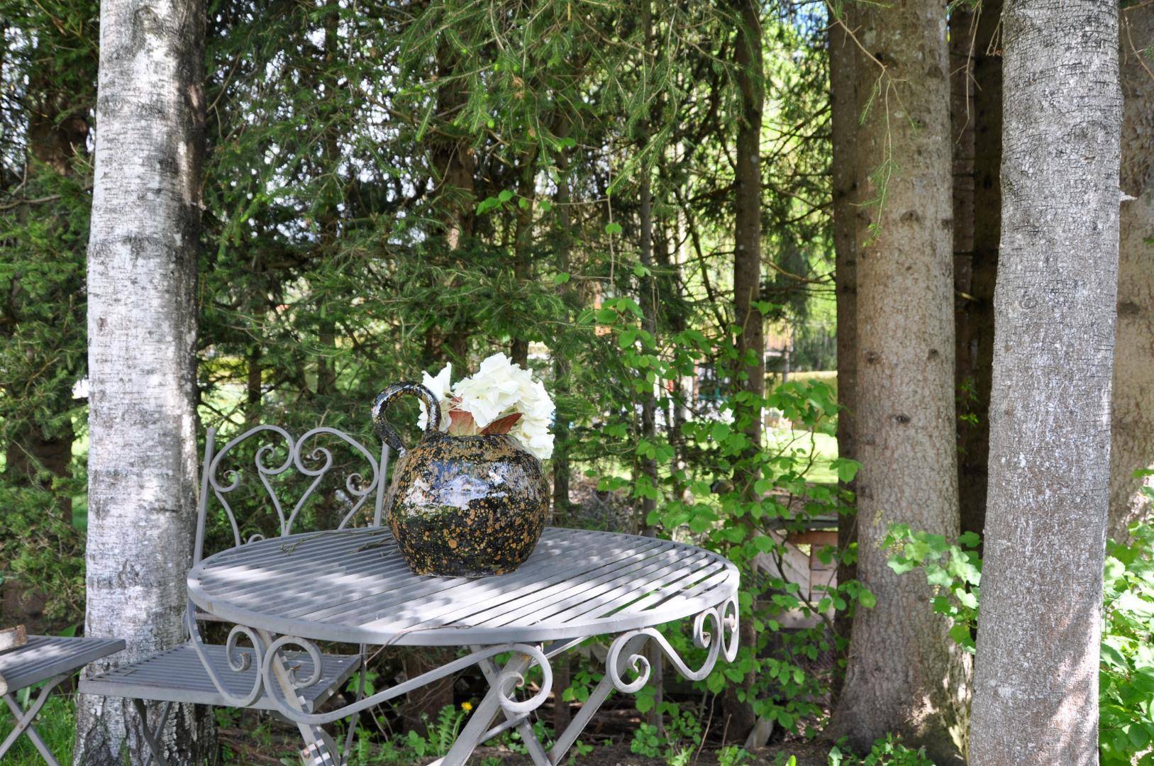 Gemütlicher Sitzbereich im Garten unter Bäumen mit schmiedeeisernen Möbeln.