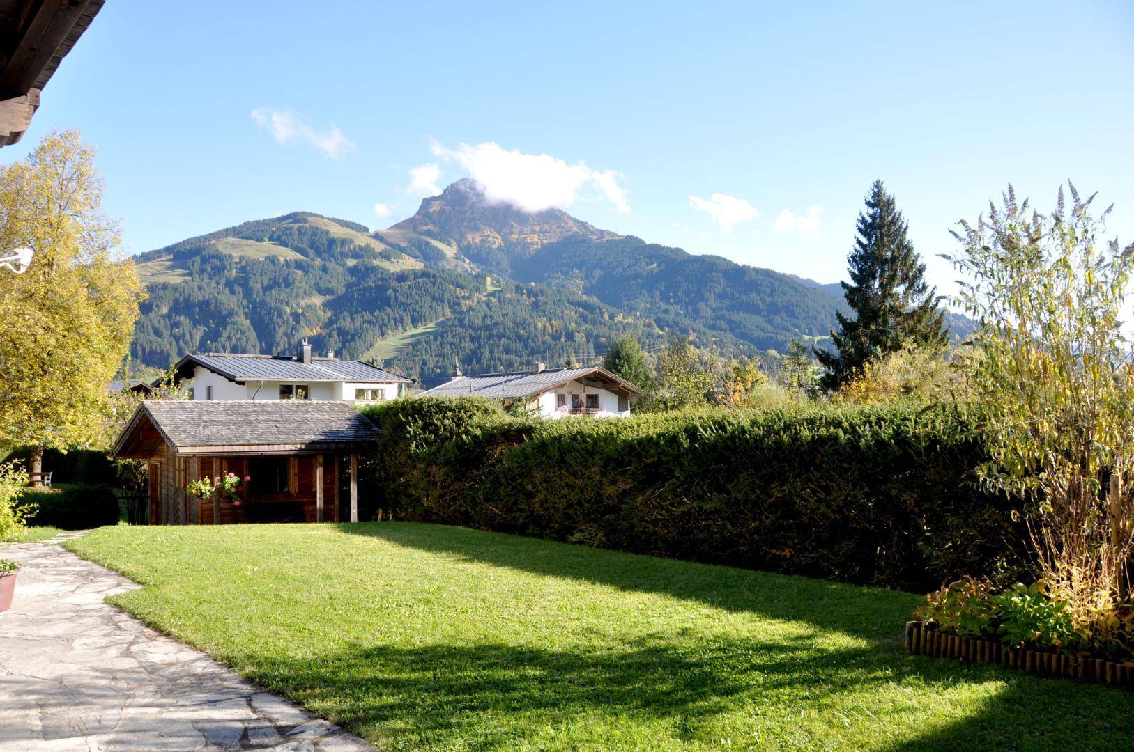 Großer Rasenbereich im Garten mit Hecke, Gartenhaus und beeindruckendem Bergblick.