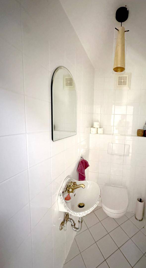 Kleines Gäste-WC mit weißer Fliesenwand, Waschbecken und wandmontierter Toilette.