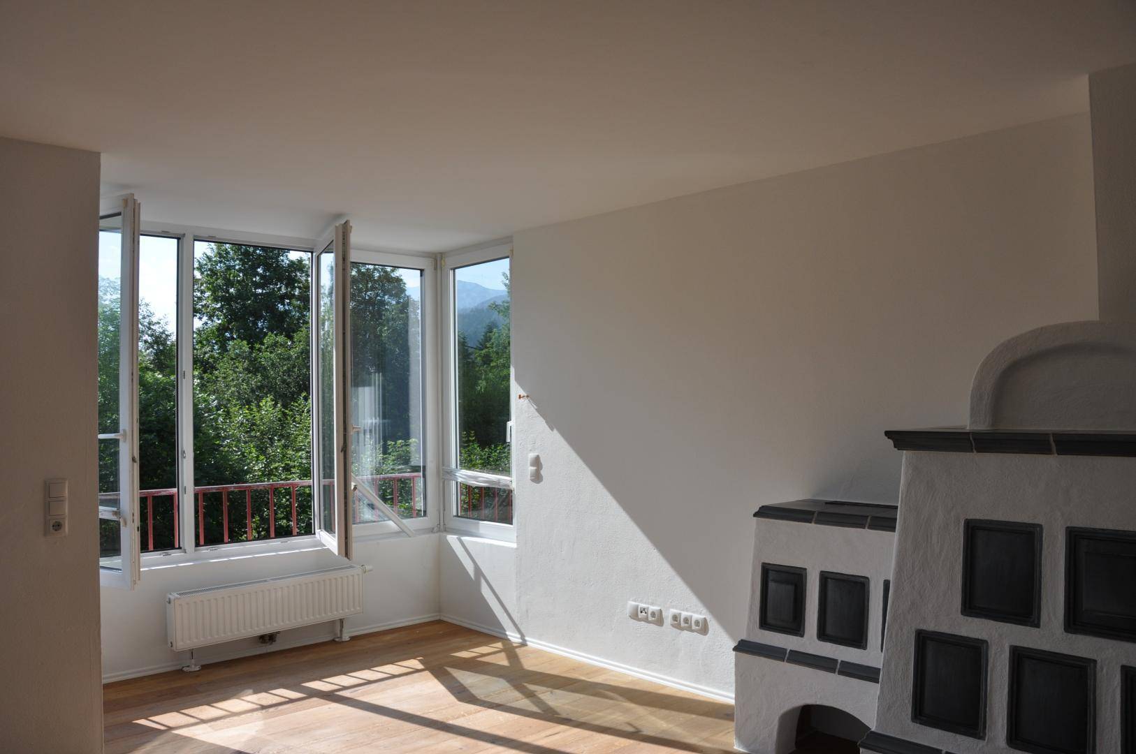 Lichtdurchflutetes Wohnzimmer mit Kachelofen, Holzboden und weitem Blick ins Grüne.