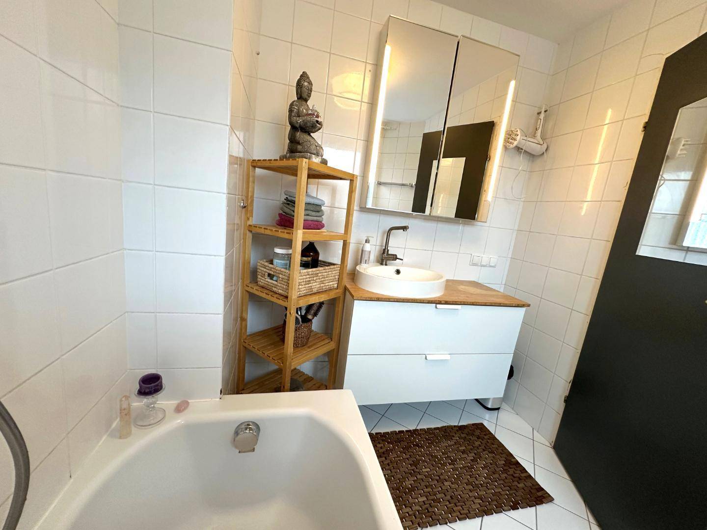 Modernes Badezimmer mit Badewanne, Waschtisch und Spiegelschrank, komplett gefliest.