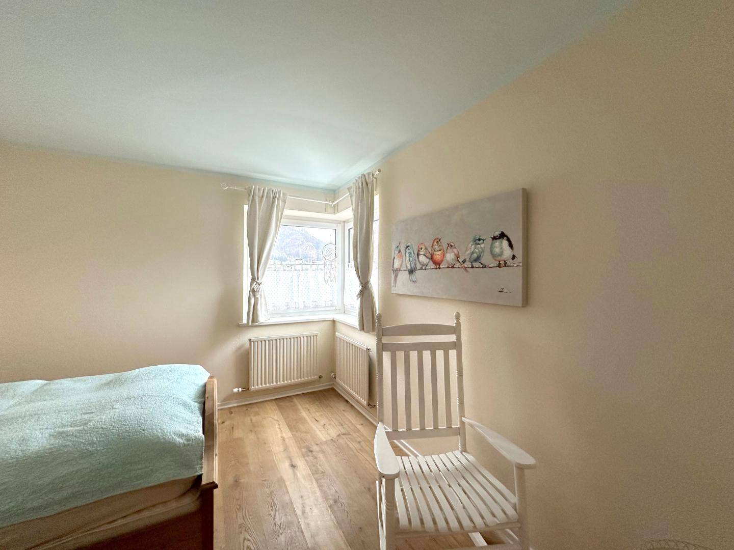 Gemütliches Schlafzimmer mit Holzboden, hellen Wänden und einem Fenster mit Ausblick.