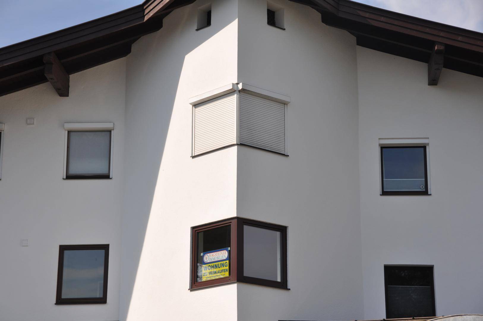 Detailansicht der Gebäudefassade mit Fenstern, Rollläden und einem "Wohnung zu verkaufen"-Schild.