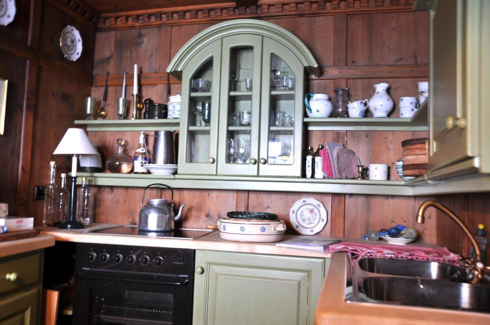 Rustikale Küche mit holzgetäfelten Wänden, grünen Schränken und integriertem Ofen im Landhausstil.