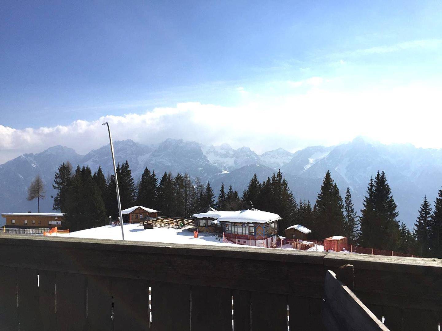 Panoramablick auf schneebedeckte Berge und Nadelwälder unter blauem Himmel mit Sonnenschein.