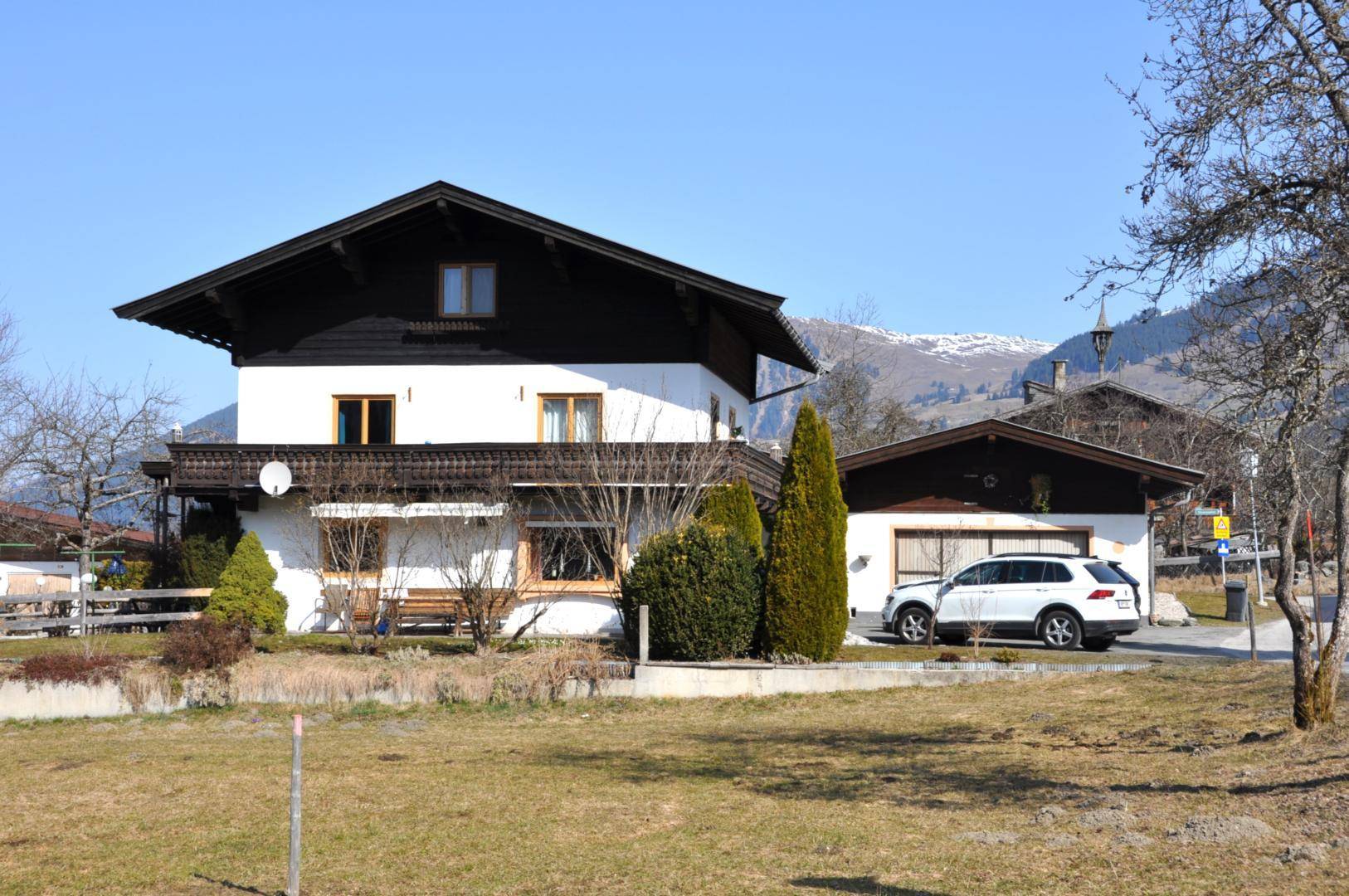 Vorderansicht des Hauses mit Parkplatz und malerischer Bergkulisse im Hintergrund.