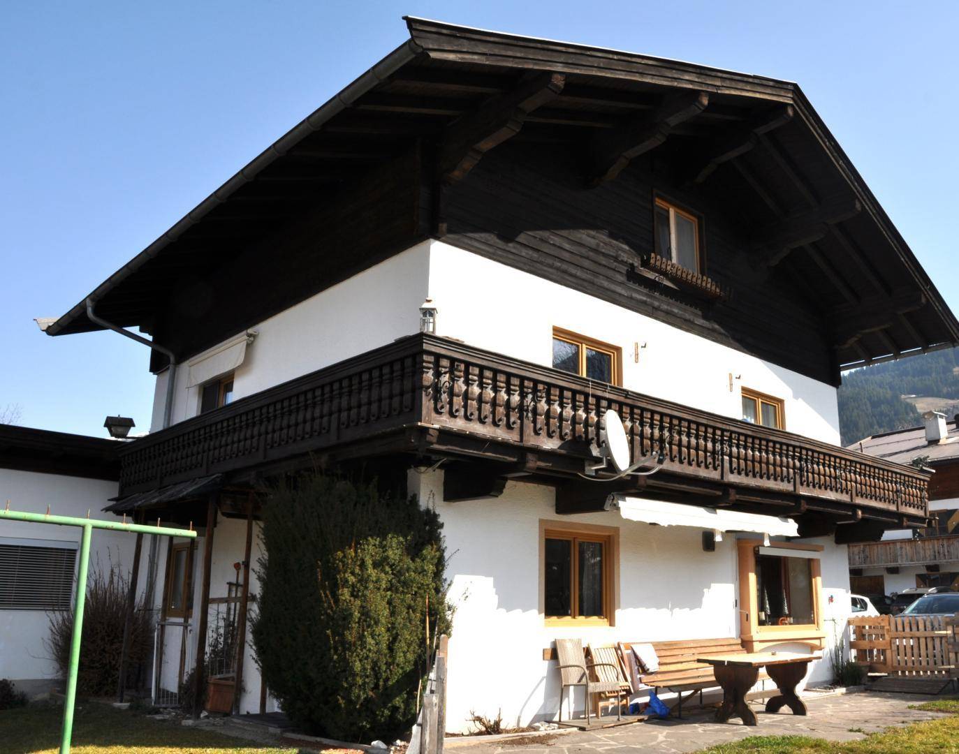 Seitenansicht des Hauses mit traditionellem Holzbalkon und kleinem Gartenbereich.
