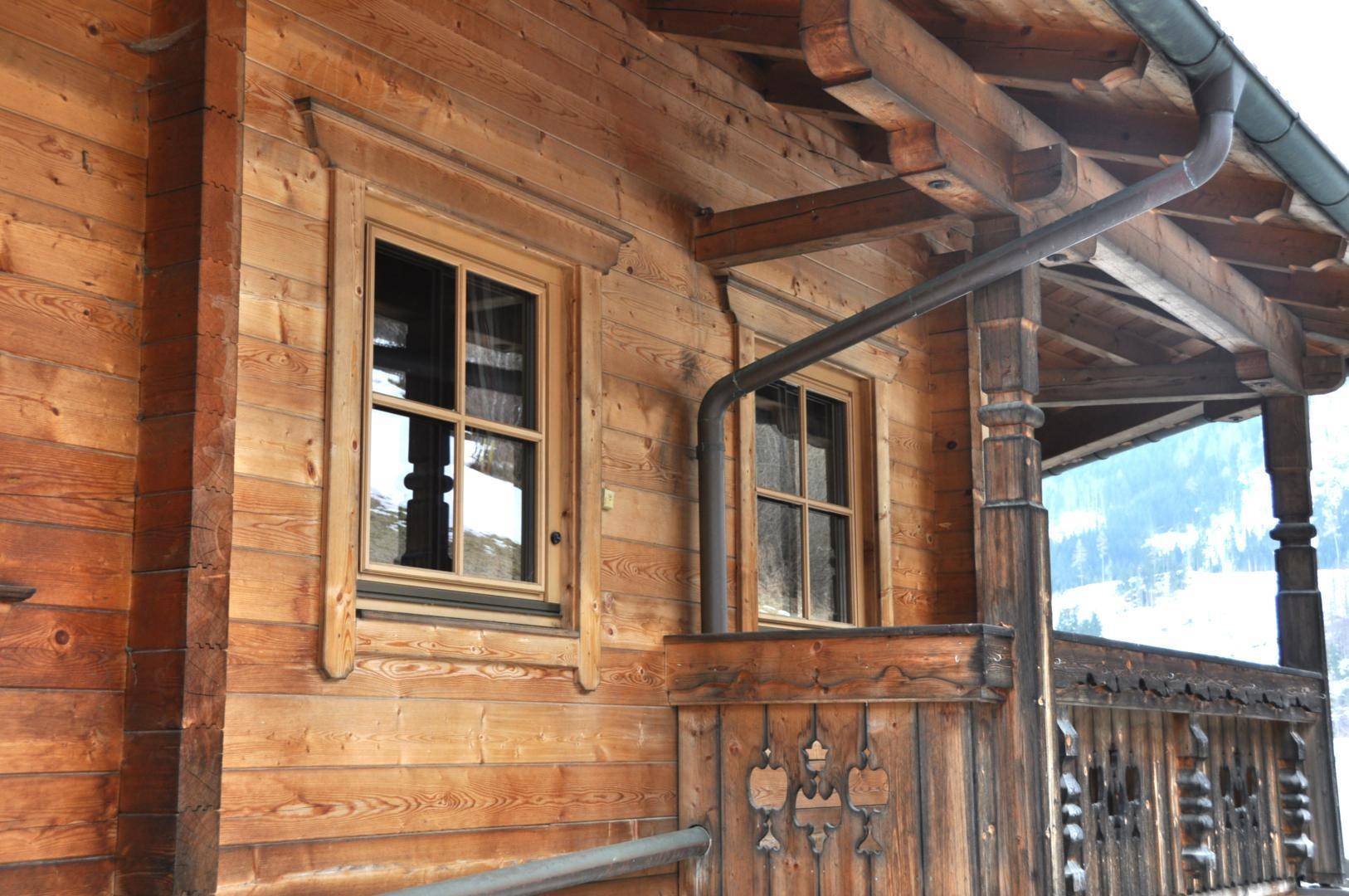 Detail der Holzfassade mit traditionellen Fenstern und Dachrinne im alpinen Baustil.