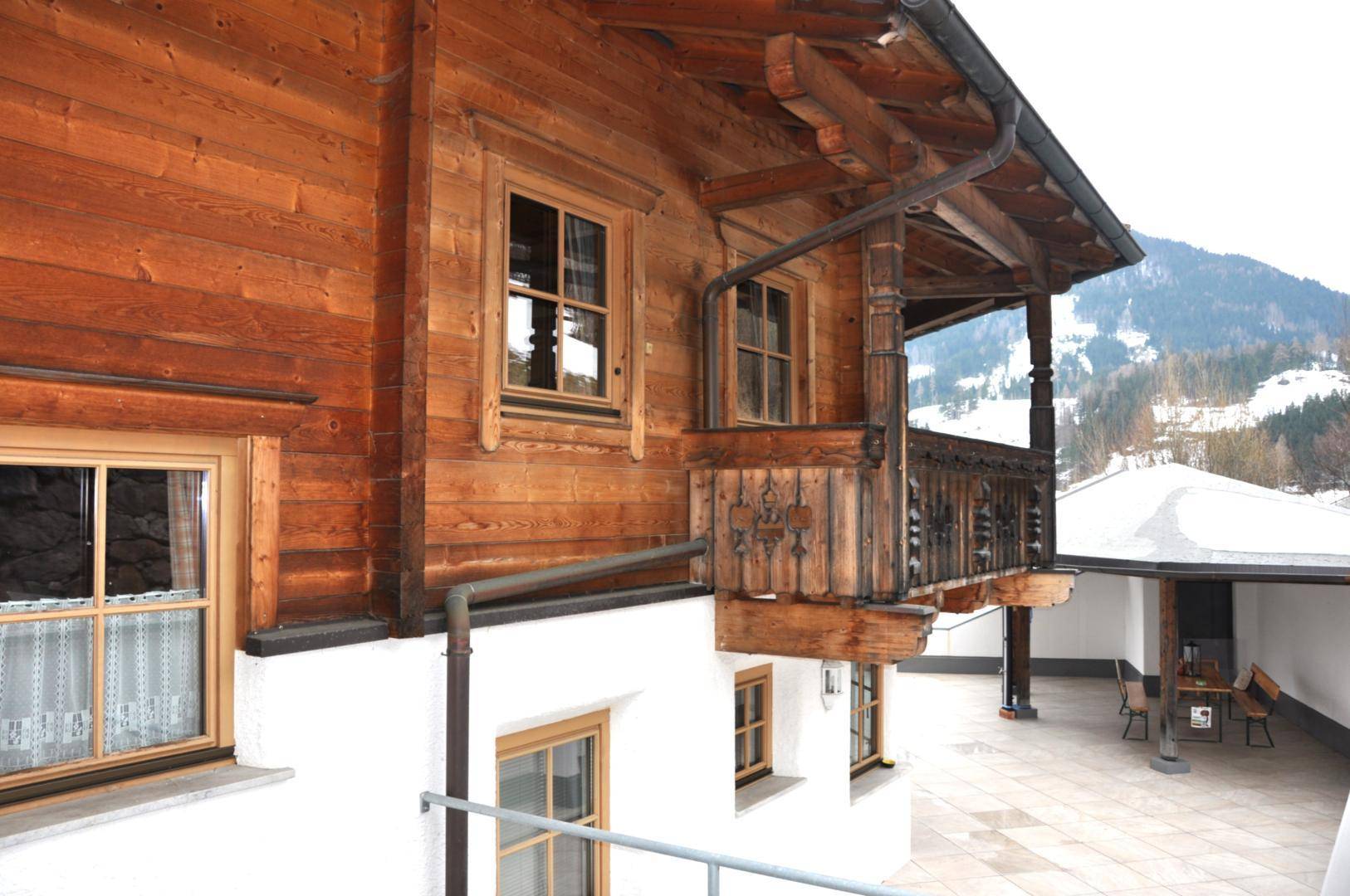 Seitliche Ansicht des Holzhauses mit großer gepflasterter Terrasse und Sitzbereich.