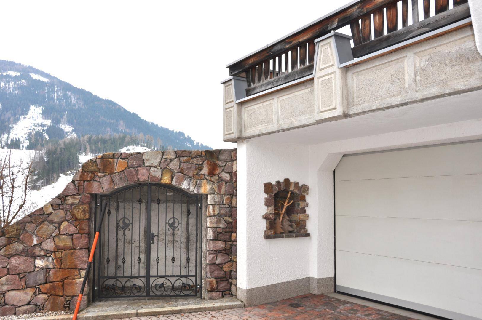 Garageneinfahrt mit automatischem Tor und rustikaler Steinmauer mit schmiedeeisernem Tor.